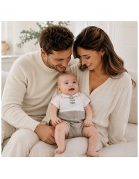 Neonato con pagliaccetto estivo panna e tortora in lino e cotone fotografato in un contesto familiare con mamma e papà.