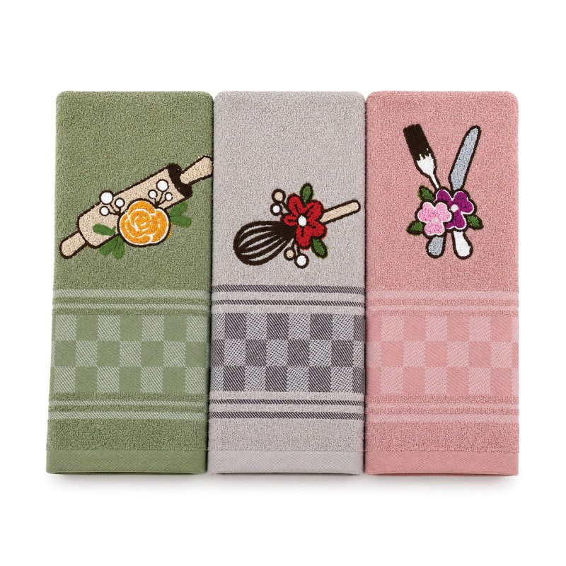 Set strofinacci cucina in cotone e spugna leggermente aperti su piano cucina con dettagli ricamati e colori pastello.