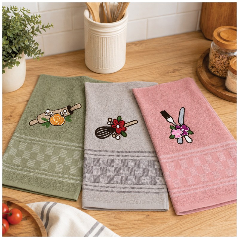 Tris di strofinacci cucina in spugna con ricami utensili da cucina nei colori verde salvia, beige e rosa su tavolo in legno.