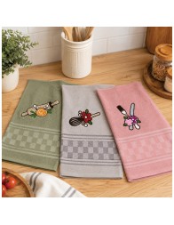 Set of three embroidered terry kitchen towels in sage green, beige and pink displayed on a wooden kitchen table.